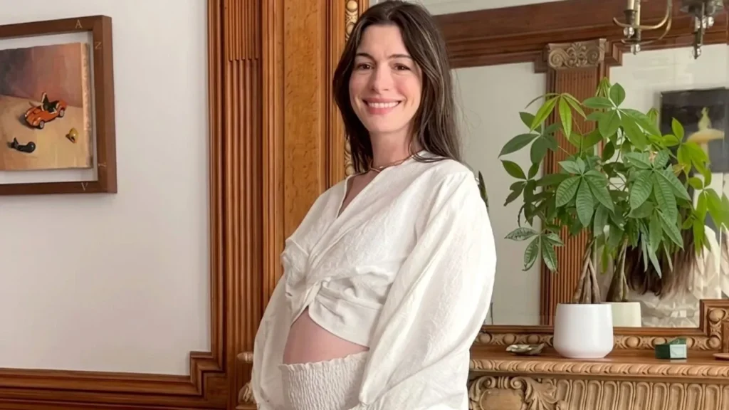 A beautiful black-and-white portrait of actress Anne Hathaway smiling and cradling her baby bump.