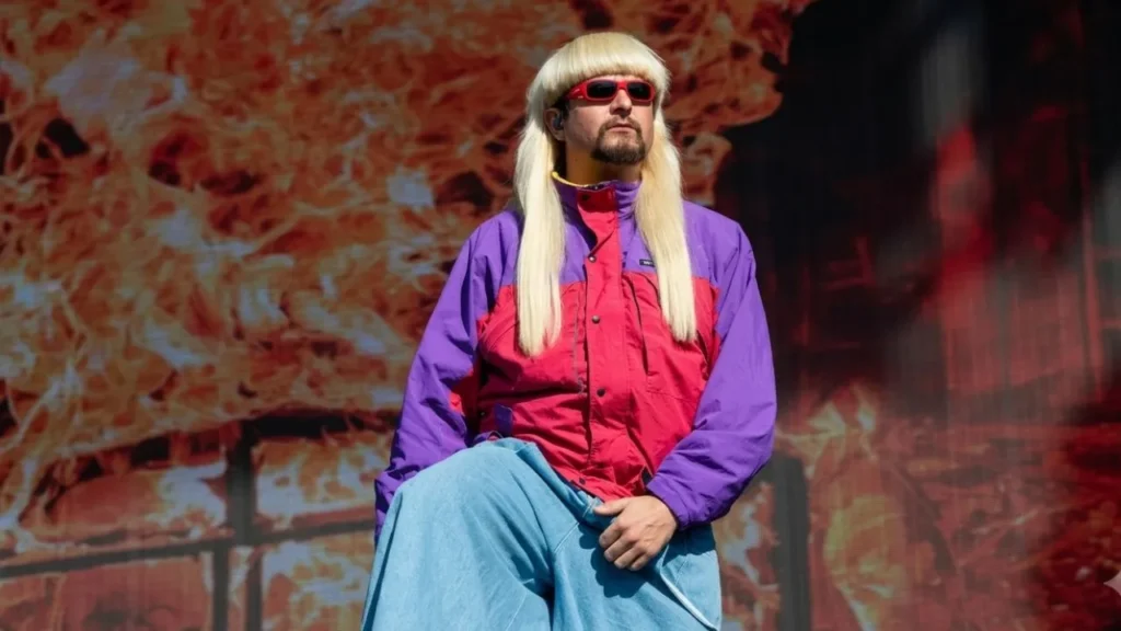 Alt-pop singer Oliver Tree smiling in his signature retro sunglasses and bowl cut hairstyle.
