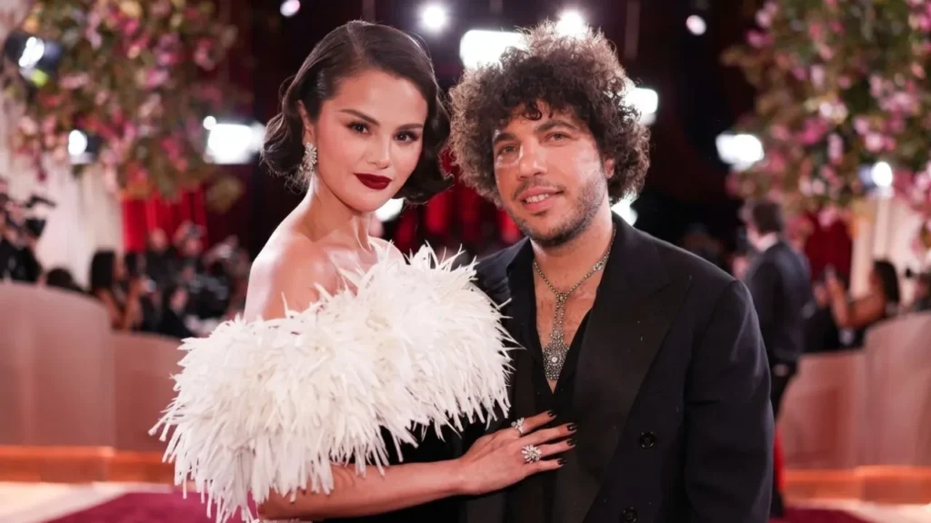 A candid, unfiltered photo of Selena Gomez and producer Benny Blanco laughing together in a kitchen.